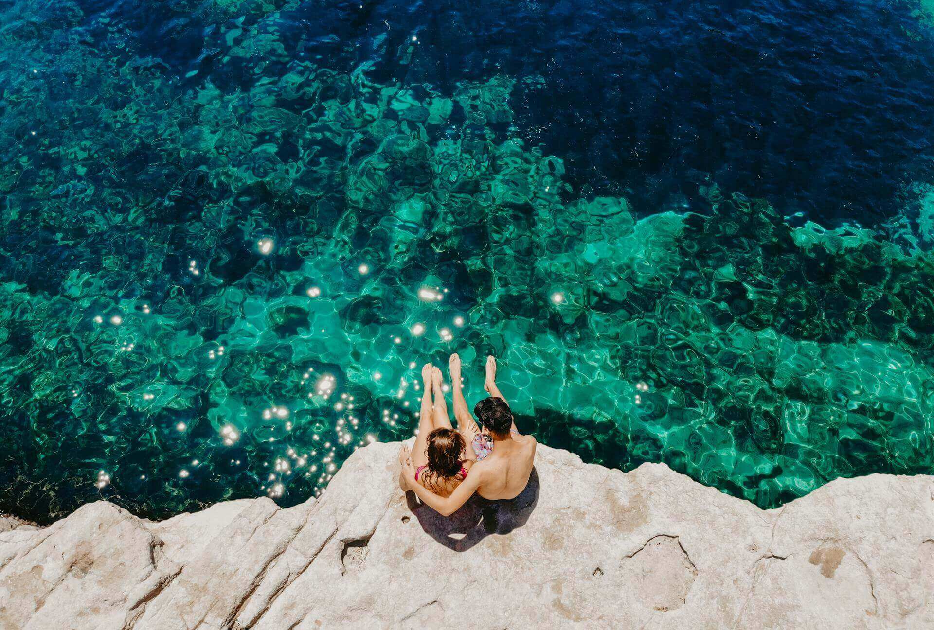 Para spacerująca brzegiem turkusowego morza o zachodzie słońca, romantyczna sceneria idealna na wakacje.